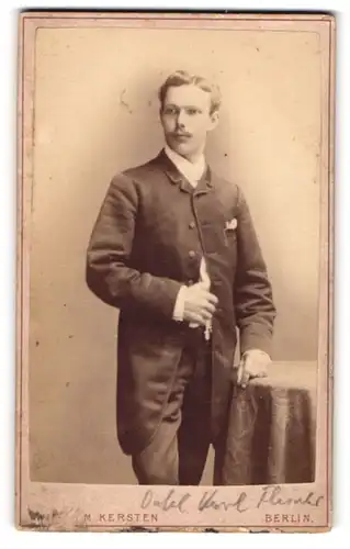 Fotografie Wilhelm Kersten, Berlin S.W. Krausen-Str. 40, Mann im Mantel steht neben einem bedeckten Tisch