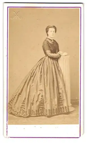Fotografie Maes, Anvers, 1. Rue des Aveugles, Eine Frau mit übergrossem Kleid steht an einer Säule