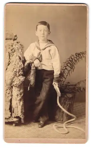 Fotografie unbekannter Fotograf und Ort, Kleiner Junge im weissen Hemd mit einem Seil in der Hand
