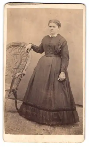 Fotografie unbekannter Fotograf und Ort, Dame im Sonntagskleid neben einem Stuhl