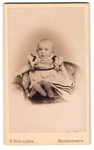 Fotografie H. Schilgen, Schöningen, am Bahnhof, Kleines niedliches Baby im Kleid auf einem Sessel