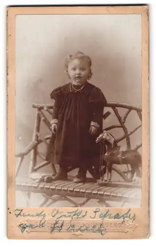 Fotografie Georg Schönau, Nürnberg, Bayreuther-Str. 20, Kleines Baby im schwazen Kleid auf einer Bank