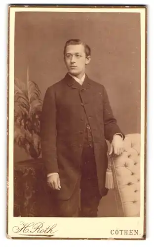Fotografie H. Roth, Cöthen, Promendae 27, Junger Mann mit Brille mit der Hand am Sessel