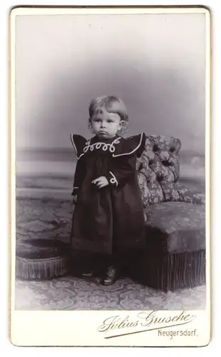 Fotografie Julius Grusche, Neugersdorf, Süsses Baby im schwarzen Kleid neben einem kleinen Sessel