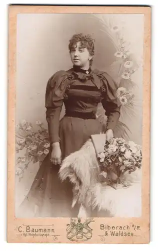 Fotografie C. Baumann, Biberach a. R., Dame im ausgeladenen Kleid mit Blumenstrauss