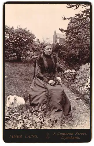 Fotografie James Laing, Clydebank, Ansicht Clydebank, Frau um bestickten Kleid posiert im Garten mit ihrem Hund