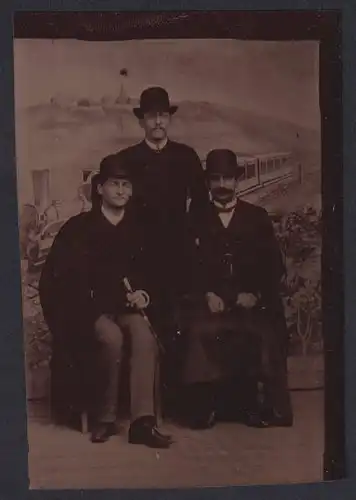 Fotografie Ferrotypie drei ältere Herren in Anzügen mit Flanierstock und Melone vor einer Studiokulisse