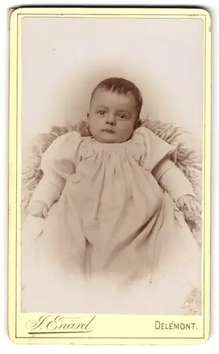 Fotografie J. Enard, Delemont, Kleines Baby im weissen Kleid auf einem Schaffell