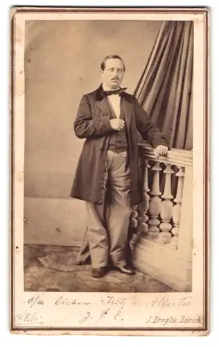 Fotografie J. Broglie, Zürich, Portrait charmanter Mann im Anzug am Geländer stehend