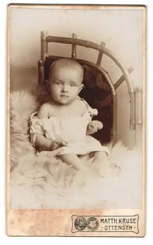 Fotografie Matth. Kruse, Ottensen, Papenstr. 7, Portrait niedliches Baby im weissen Hemdchen auf Fell sitzend