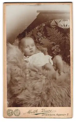 Fotografie Matth. Kruse, Ottensen, Papenstr. 7, Portrait niedliches Baby im Hemdchen auf Fell liegend