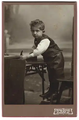 Fotografie Bernh. Krause, Kiel, junger Knabe als Tischler mit Hobel und Schürze am Werkstück