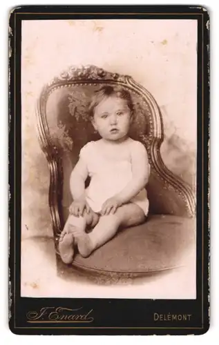 Fotografie J. Enard, Delemont, Kleinkind in weissem Kleid, in verschnörkeltem Stuhl sitzend