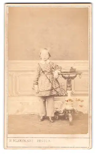Fotografie H. Blanckart, Hasselt, Mädchen im kariertem Kleid an Tischchen angelehnt