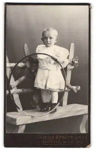 Fotografie Berghausen, Borbeck, Markt 12, kleiner Junge im weissen Kleidchen mit Spielreif