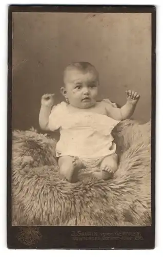 Fotografie J. Saurin, Berlin-Weissensee, Berliner Allee 230, Portrait süsses Baby im Hemdchen auf einem Fell sitzend