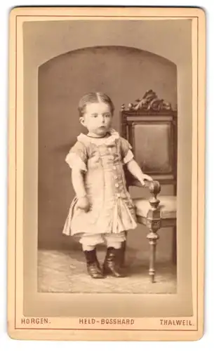 Fotografie Held-Bosshard, Horgen am Zürichsee, Portrait süsses Mädchen im Kleidchen am Stuhl stehend