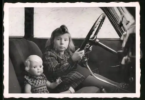 Fotografie Auto, Mädchen nebst Puppe am Steuer sitzend