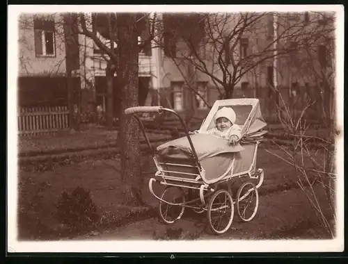 Fotografie Baby mit weisser Mütze im Kinderwagen