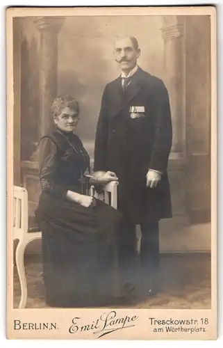 Fotografie Emil Lampe, Berlin, älteres Paar, Herr im Anzug mit Ordenspange und Kaiser Wilhelm Bart