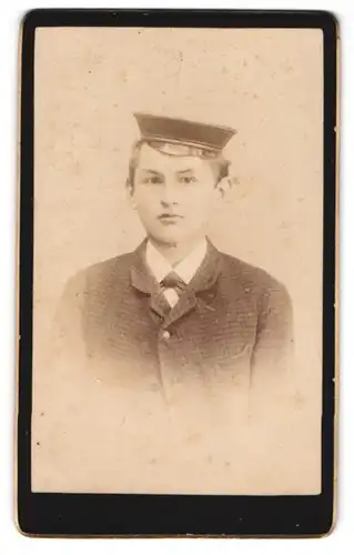 Fotografie unbekannter Fotograf und Ort, junger Student im karierten Anzug mit Schirmmütze samt Couleur