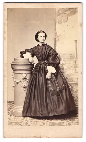 Fotografie F. Brandseph, Stuttgart, Portrait junge Frau im dunklen Kleid mit Halskette vor Studiokulisse, Jubiläumssäule