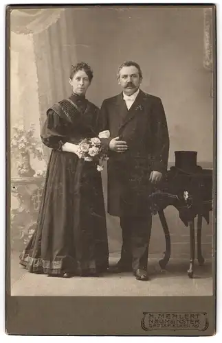 Fotografie H. Mehlert, Neumünster, Brautpaar im schwarzen Kleid und im Anzug nebst Zylinder