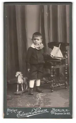 Fotografie Eduard Krause, Berlin, niedlicher Knabe im Anzug mit Segelschiff und Spielzeug Pferd