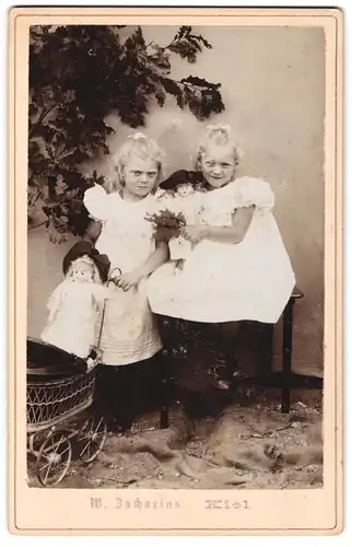 Fotografie W. Zacharias, Kiel, Portrait niedliche blonde Mädchen in Kleidern mit Puppe und Puppenwagen