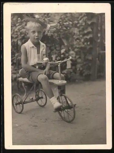 Fotografie Blonder Knabe mit Hut auf Dreirad sitzend