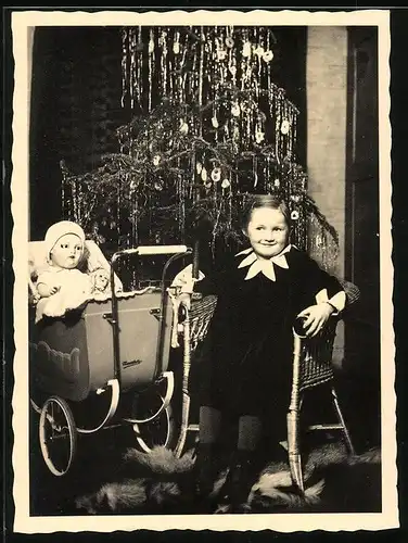 Fotografie Weihnachten, glückliches Mädchen mit Puppe & Puppenwagen vor Weihnachtsbaum