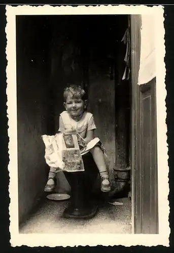 Fotografie Knabe mit Zeitung auf der Toilette sitzend