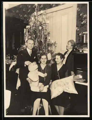Fotografie Weihnachten, hübsche Frau mit Teddybär im kreise der Familie vor Weihnachtsbaum sitzend