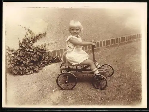 Fotografie Spielzeug, blondes Kleinkind sitzt im Tretauto