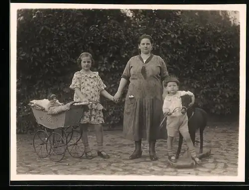 Fotografie Mädchen mit Puppe & Puppenwagen, Knabe mit Spielzeug-Pferd flankieren beleibte Mutter