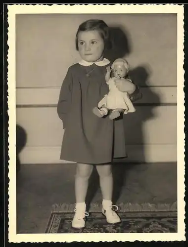 Fotografie Mädchen im Kleidchen hält Puppe im Arm