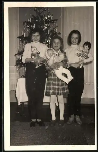Fotografie Weihnachten, glückliche Mädchen mit Puppe vor dem Weihnachtsbaum stehend