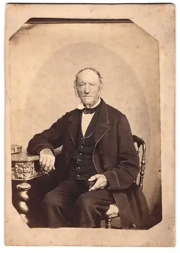 Fotografie unbekannter Fotograf und Ort, älterer Herr im Anzug mit gepunkteter Weste sitzend im Atelier