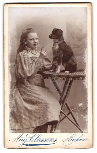 Fotografie Aug. Classens, Aachen, junges Mädchen im karierten Kleid mit ihrem Hund auf dem Tisch, mach Sitz