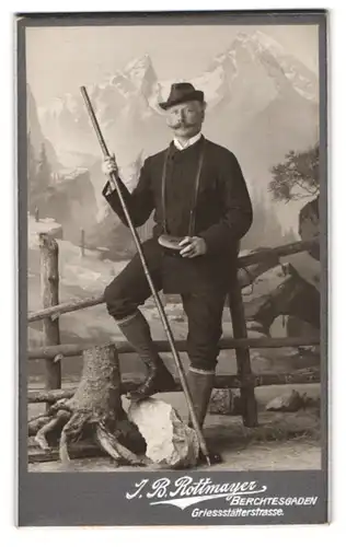 Fotografie J. B. Rottmayer, Berchtesgaden, Portrait Herr als Wanderer mit Fernglas Tasche und Wanderstock, Studiokulisse