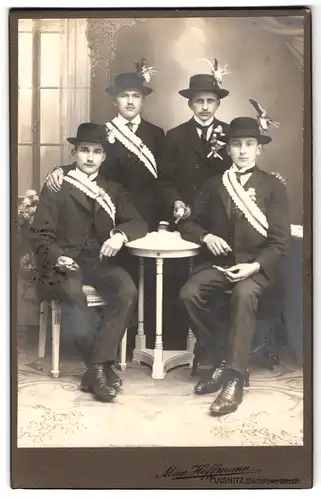 Fotografie Max Hoffmann, Pulsnitz, Portrait vier junge Herren zu ihrer Musterung in Anzügen mit Schärpe und Federhut