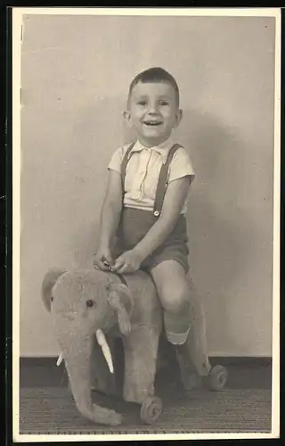 Fotografie Spielzeug, lachender Knabe auf Spielzeug-Elefant sitzend