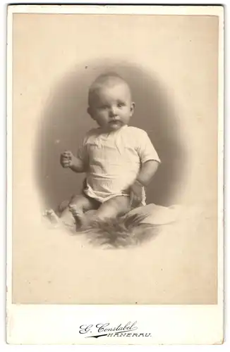 Fotografie G. Constabel, Hanerau, Süsses Kleinkind im Hemd sitzt auf Fell
