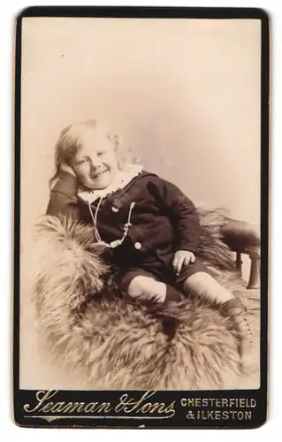 Fotografie Seaman & Sons, Chesterfield, Portrait süsser blonder Bube auf einem Fell sitzend