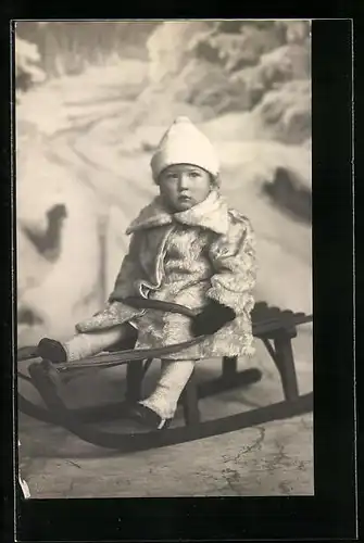 AK Mädchen sitzt mit Wollmütze und Pelzmantel auf einem Schlitten