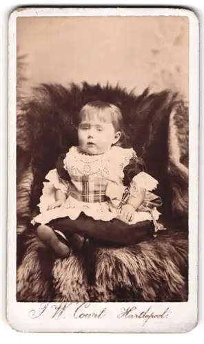 Fotografie J. W. Court, Hartlepool, Northgate St., Portrait blondes Mädchen im Kleidchen auf Fell sitzend