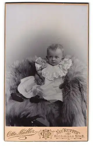 Fotografie Otto Müller, Neuruppin, Wichmann Str. 8, Süsses Kleinkind im Rüschenkleid sitzt auf Fell
