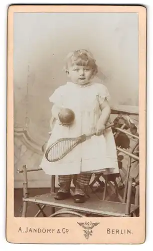 Fotografie A. Jandorf & Co., Berlin, C. Spittelmarkt 16 /17, Kleines Mädchen im weissen Kleid mit Tennischläger und Ball