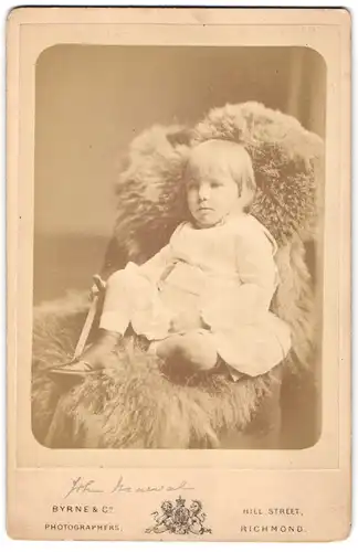 Fotografie Byrne & Co., Richmond, Hill Street, Kind in weisser Kleidung sitzt auf Fell