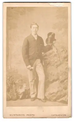 Fotografie Humphreys, Carnarvon, Castle Square, Portrait charmanter junger Mann mit Zylinder in der Hand